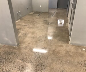 A hallway with polished concrete floors, gray walls, exposed wall outlets, and visible patches or markings on the surface. The shiny epoxy flooring Connecticut reflects overhead lighting for a clean, modern appearance. A hallway with polished concrete floors, gray walls, exposed wall outlets, and visible patches or markings on the surface. The shiny epoxy flooring Connecticut reflects overhead lighting for a clean, modern appearance.