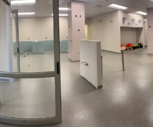 A spacious, empty room with light gray industrial floor coating, white walls, glass doors, exposed outlets, and a few construction materials and tools scattered around, suggesting ongoing renovation or setup. A spacious, empty room with light gray industrial floor coating, white walls, glass doors, exposed outlets, and a few construction materials and tools scattered around, suggesting ongoing renovation or setup.