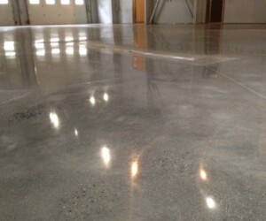 A close-up view of a smooth, polished industrial floor coating inside a large, empty commercial space with reflections of overhead lights on the surface. A close-up view of a smooth, polished industrial floor coating inside a large, empty commercial space with reflections of overhead lights on the surface.