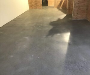 A smooth, polished concrete floor with industrial floor coating in a room with white and plywood walls, reflecting light and shadows. The area appears to be under construction or renovation. A smooth, polished concrete floor with industrial floor coating in a room with white and plywood walls, reflecting light and shadows. The area appears to be under construction or renovation.