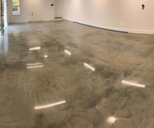 A spacious garage with smooth, polished anti-slip epoxy floors, white walls, and fluorescent ceiling lights reflected on the surface. The garage door is partially visible on the left, with windows letting in natural light. A spacious garage with smooth, polished anti-slip epoxy floors, white walls, and fluorescent ceiling lights reflected on the surface. The garage door is partially visible on the left, with windows letting in natural light.