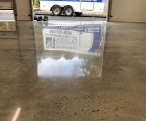 A polished concrete floor in a garage reflects the open door and a parked Everlast Flooring trailer outside, with trees visible in the background—ideal for those seeking durable epoxy flooring Connecticut solutions. A polished concrete floor in a garage reflects the open door and a parked Everlast Flooring trailer outside, with trees visible in the background—ideal for those seeking durable epoxy flooring Connecticut solutions.