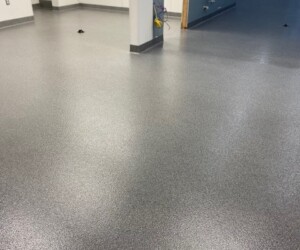A room with light gray speckled epoxy flooring Connecticut and white walls, featuring several columns and unfinished electrical outlets, suggesting ongoing construction or renovation. A room with light gray speckled epoxy flooring Connecticut and white walls, featuring several columns and unfinished electrical outlets, suggesting ongoing construction or renovation.