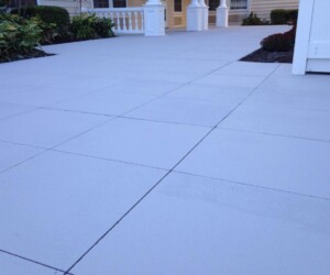 A close-up view of a clean, light-colored tiled outdoor patio, bordered by landscaped plants and white fencing, showcases the durability found in industrial floor coating, with parts of a house and porch visible in the background. A close-up view of a clean, light-colored tiled outdoor patio, bordered by landscaped plants and white fencing, showcases the durability found in industrial floor coating, with parts of a house and porch visible in the background.