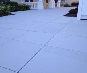 A close-up view of a clean, light-colored tiled outdoor patio, bordered by landscaped plants and white fencing, showcases the durability found in industrial floor coating, with parts of a house and porch visible in the background. A close-up view of a clean, light-colored tiled outdoor patio, bordered by landscaped plants and white fencing, showcases the durability found in industrial floor coating, with parts of a house and porch visible in the background.