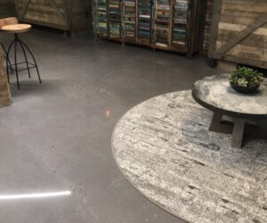 Industrial-style room with an anti-slip epoxy floor, a round area rug, low coffee table with a plant, rustic wooden cabinet, two barn doors, bar stool, and a wall-mounted TV above the cabinet. Industrial-style room with an anti-slip epoxy floor, a round area rug, low coffee table with a plant, rustic wooden cabinet, two barn doors, bar stool, and a wall-mounted TV above the cabinet.