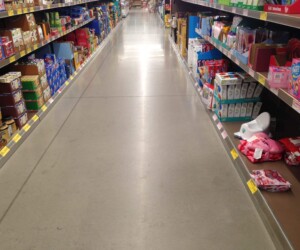 A grocery store aisle with shelves on both sides stocked with various packaged food items and household products. The organized shelves stand above a clean, shiny anti-slip epoxy floor for added safety and durability. A grocery store aisle with shelves on both sides stocked with various packaged food items and household products. The organized shelves stand above a clean, shiny anti-slip epoxy floor for added safety and durability.