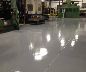 A clean, glossy, gray USDA approved flooring coats the factory floor, with large industrial machines and worktables in the background inside a spacious industrial facility. A clean, glossy, gray USDA approved flooring coats the factory floor, with large industrial machines and worktables in the background inside a spacious industrial facility.