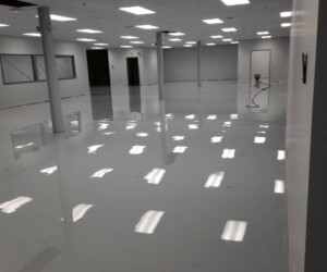 A large, empty room with a shiny, freshly finished gray epoxy floor—ideal for industrial floor coating—with white walls, support columns, and ceiling lights reflecting on the smooth surface. A large, empty room with a shiny, freshly finished gray epoxy floor—ideal for industrial floor coating—with white walls, support columns, and ceiling lights reflecting on the smooth surface.