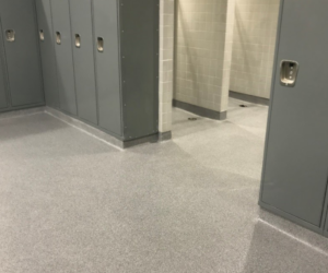 A clean locker room with gray metal lockers and tiled walls. The shiny, light gray floor features industrial floor coating, and private shower or changing stalls are visible in the background. A clean locker room with gray metal lockers and tiled walls. The shiny, light gray floor features industrial floor coating, and private shower or changing stalls are visible in the background.