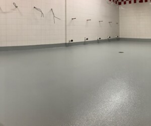 A large, empty room with white tiled walls and a smooth, industrial floor coating. Wires extend from the walls, suggesting ongoing construction or renovation. A large, empty room with white tiled walls and a smooth, industrial floor coating. Wires extend from the walls, suggesting ongoing construction or renovation.