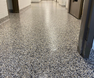 A low-angle view of a hallway with speckled, polished resinous flooring CT, white walls, and several open doors along the corridor. The hallway appears clean and brightly lit. A low-angle view of a hallway with speckled, polished resinous flooring CT, white walls, and several open doors along the corridor. The hallway appears clean and brightly lit.