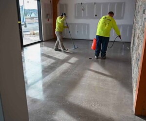 Two workers in yellow shirts clean and polish a shiny USDA approved flooring inside a building with unfinished walls, near large windows and wooden beams. Two workers in yellow shirts clean and polish a shiny USDA approved flooring inside a building with unfinished walls, near large windows and wooden beams.