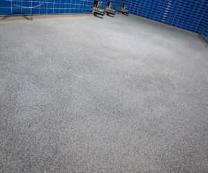 Room with blue tiled walls and a newly installed speckled gray USDA approved flooring, with exposed pipes visible along the far side of the wall. Room with blue tiled walls and a newly installed speckled gray USDA approved flooring, with exposed pipes visible along the far side of the wall.