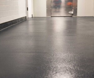 A clean, smooth, dark gray anti-slip epoxy floor in a hallway with white tiled walls and a metal door at the end. The photo is taken from a low angle, highlighting this USDA approved flooring’s texture and durability. A clean, smooth, dark gray anti-slip epoxy floor in a hallway with white tiled walls and a metal door at the end. The photo is taken from a low angle, highlighting this USDA approved flooring’s texture and durability.