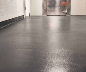 A clean, smooth, dark gray anti-slip epoxy floor in a hallway with white tiled walls and a metal door at the end. The photo is taken from a low angle, highlighting this USDA approved flooring’s texture and durability. A clean, smooth, dark gray anti-slip epoxy floor in a hallway with white tiled walls and a metal door at the end. The photo is taken from a low angle, highlighting this USDA approved flooring’s texture and durability.
