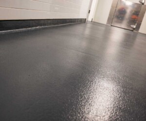 A close-up view of a clean, smooth dark gray resinous flooring CT in a hallway with white tiled walls and a metal door at the end. A close-up view of a clean, smooth dark gray resinous flooring CT in a hallway with white tiled walls and a metal door at the end.